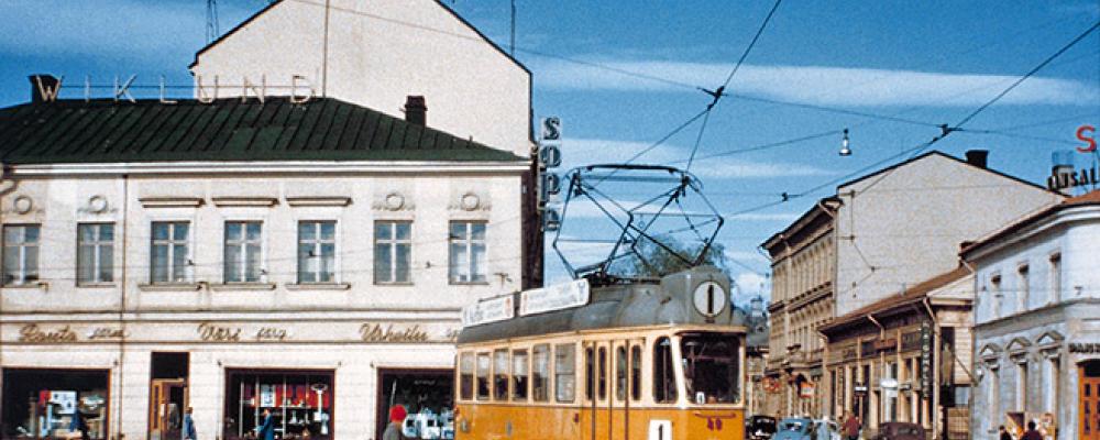 Spårvagn på Salutorget i Åbo 1959. Spårvagn nummer 49 av typen Valmet RM 2 trafikerade linje 1 när den år 1959 fotograferades vid Salutorget i Åbo. På bilden svänger vagnen i sydostlig riktning från Köpmansgatan in på Eriksgatan. Spårvägen lades ner 1972 och bussarna fick ta över transporterna. Foto: Okänd – stadinratikat.fi vid Wikipedia Common Lic.