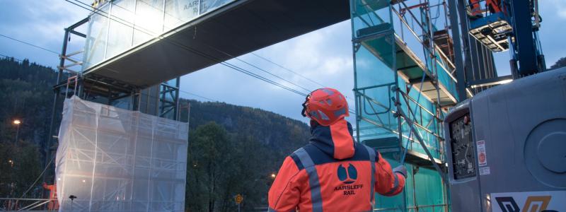 Aarsleff Rail lyfter en gångbro på plats på Evanger Station. Brokonstruktioner och hisstorn har byggts i Danmark och transporterats med lastbil till Norge.