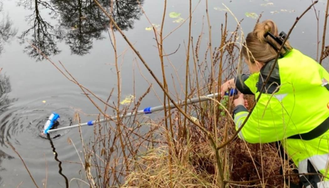 En vattenhämtare med teleskopspinne används för att samla in vattenprover en bit ut från strandkanten. Proverna skickas sedan till laboratorium för analys. Foto: Trafikverket