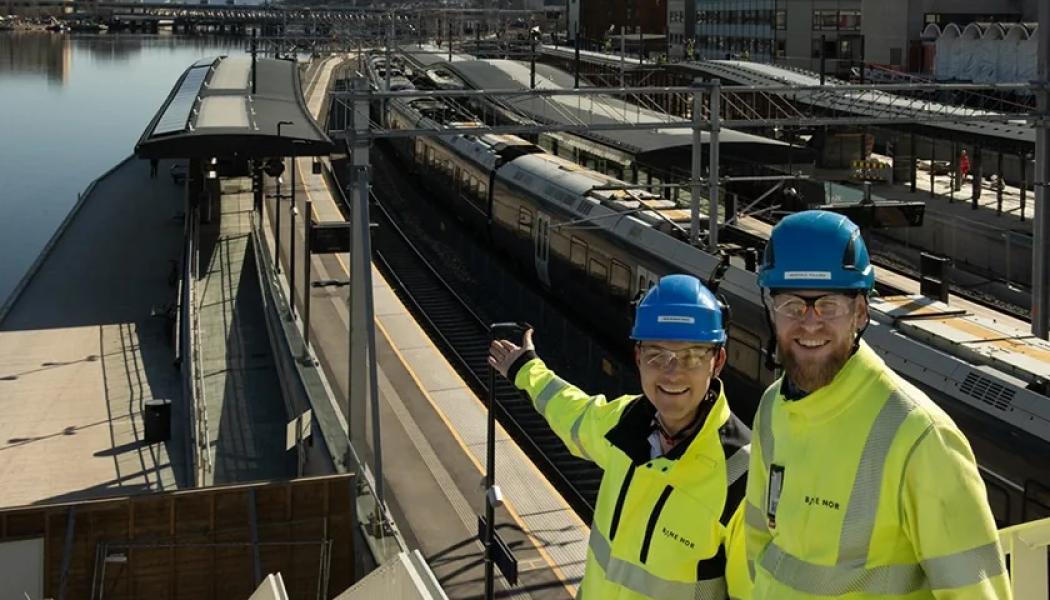 Infrastrukturarbeten vid Drammens station i Norge. Geir Boman Rinde (till vänster) och Morten E. Paulsen är båda byggledare för el på stationen. De visar glatt upp de första solpanelerna som installerades på plattformstaket vid floden.
Foto: Anne Mette Storvik, Bane NOR